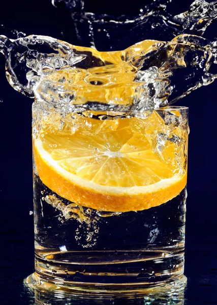 Slice of orange falling down in glass with water on deep blue — Stock Photo, Image
