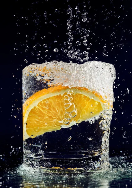 Plasterkiem pomarańczy spada w szkle z wody na granatowy — Zdjęcie stockowe