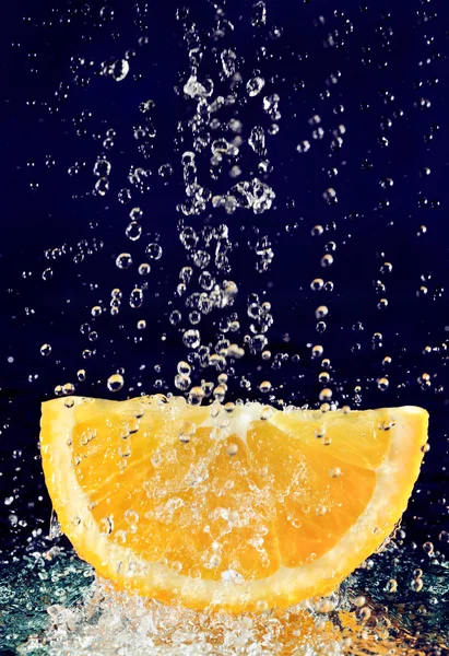 Rebanada de naranja con gotas de agua de movimiento detenido en azul profundo — Foto de Stock