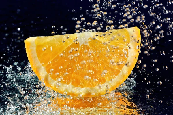 Шматочок апельсина з зупиненим рухом вода падає на глибокий синій — стокове фото