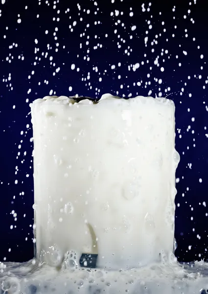 Copo cheio de leite com gotas salpicantes em azul profundo — Fotografia de Stock