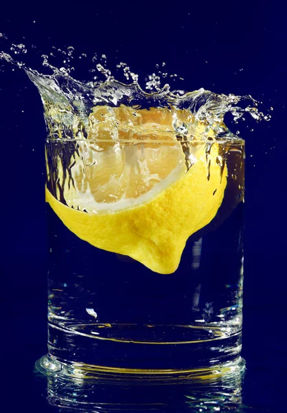 Половина лимона падает в стакан с водой на голубой — стоковое фото