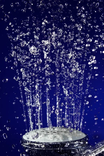 Hand douche douche met gestopt beweging water druppels op donkerblauw — Stockfoto