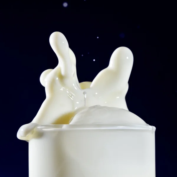 Copo de leite com gotas salpicantes em azul profundo — Fotografia de Stock
