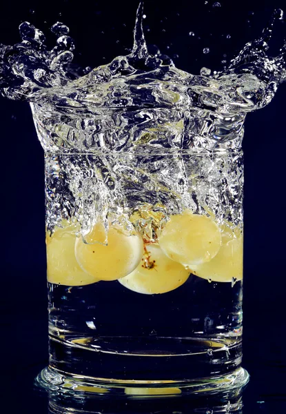 Ramo de uvas blancas cayendo en vaso con agua en la profundidad b — Foto de Stock