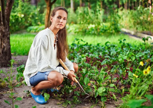 Молодая женщина с мотыгой работает в саду кровать — стоковое фото