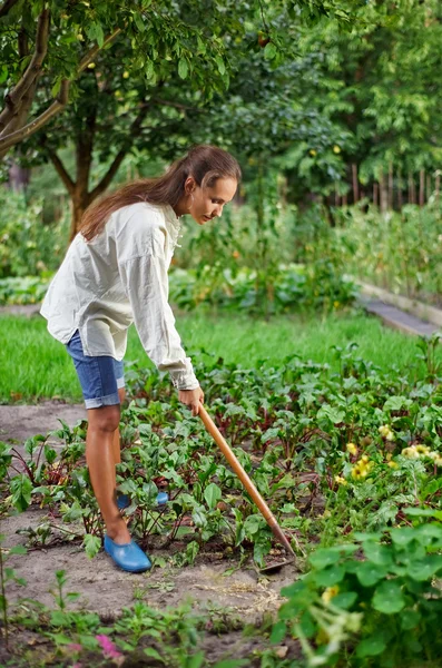 Молодая женщина с мотыгой работает в саду кровать — стоковое фото