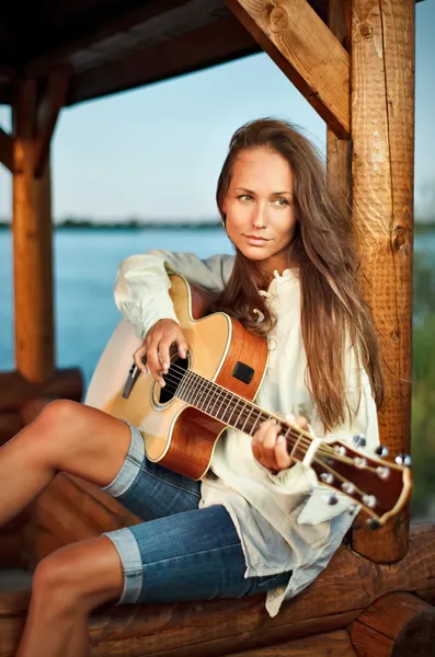 Νεαρή γυναίκα που παίζει κιθάρα σε summerhouse στο ηλιοβασίλεμα — Φωτογραφία Αρχείου