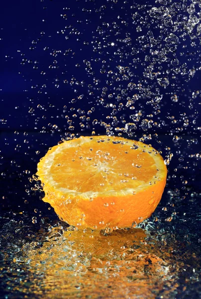 Metade de laranja com gotas de água de movimento parado em azul profundo — Fotografia de Stock
