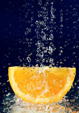 Slice of orange with stopped motion water drops on deep blue clipart