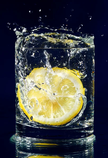 Fél citrom esik le a pohár vízzel a mély kék — Stock Fotó