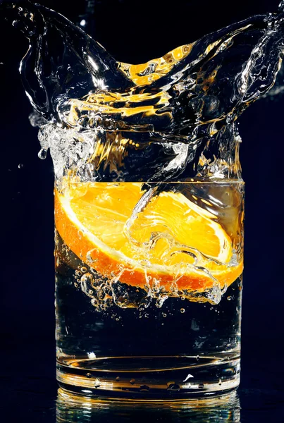 Trozo Naranja Que Cae Vaso Con Agua Sobre Azul Profundo — Foto de Stock