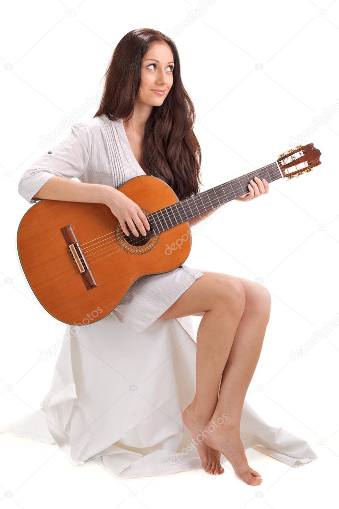 Young beautiful smiling brunette lady in white chemise playing acoustic guitar