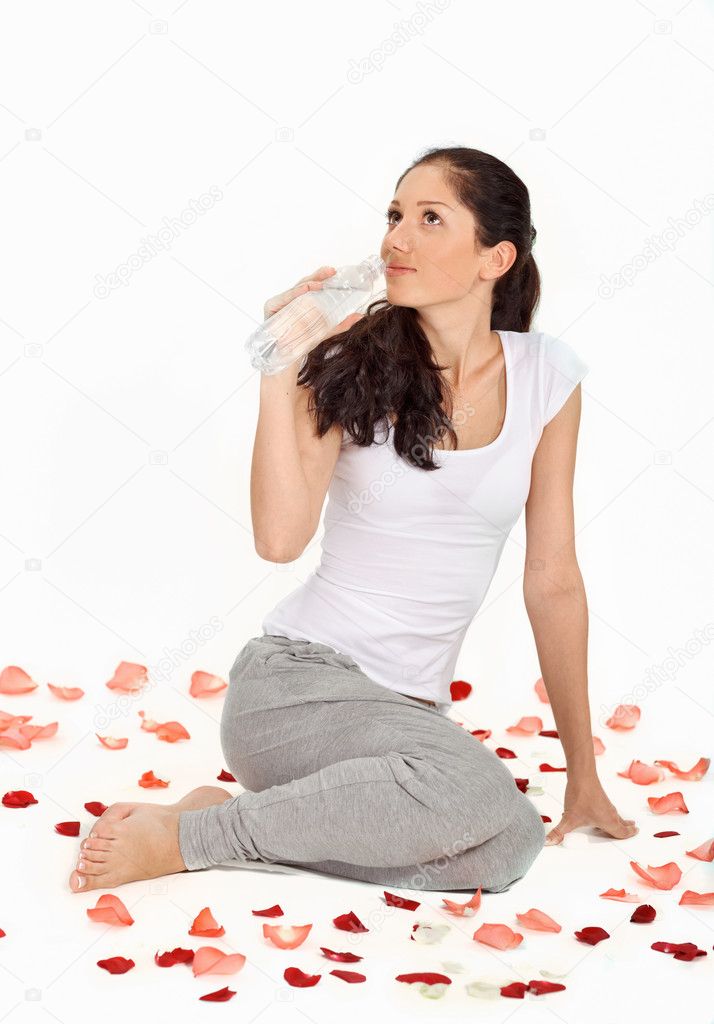 Young beautiful lady drinking gas water sitting on the floor covered with rose petals