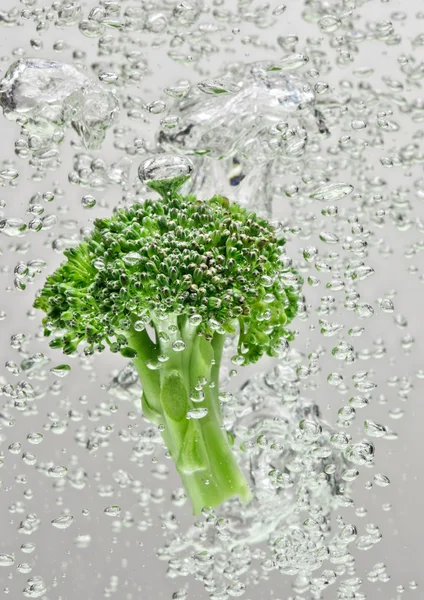 Green broccoli falling in water with air bubbles
