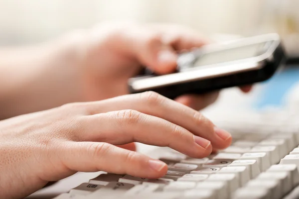 Holding phone hand typing computer keyboard — Stock Photo, Image
