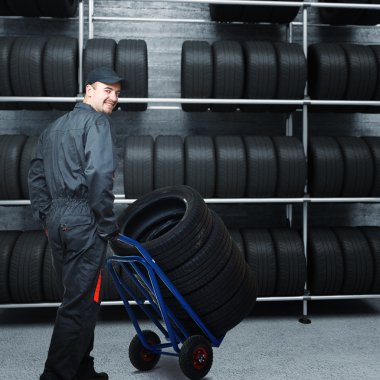 caucasian mechanic at work with tires and 3d garage background clipart