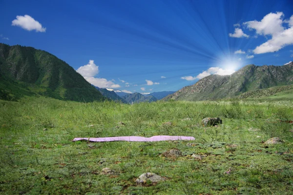 Yogamatta på gröna fält nära bergen — Stockfoto