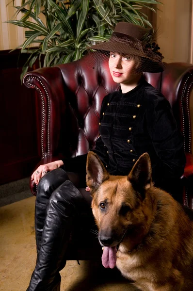 年轻女子坐在一个皮革扶手椅上 抚摸狗 — 图库照片