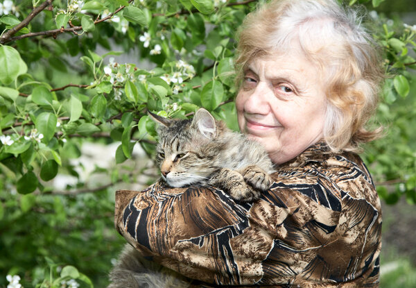 The old woman hold on hands cat against a blossoming tree
