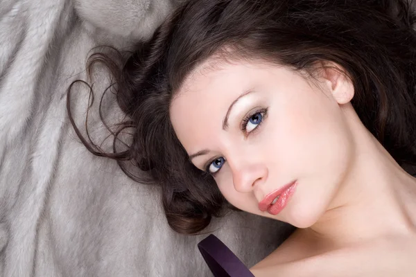 Portrait of the young woman lying on grey fur coat — Stock Photo, Image
