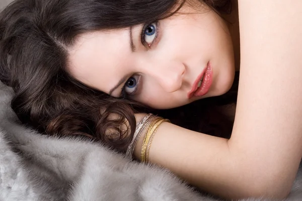 Lovely young woman lying on grey fur coat — Stock Photo, Image