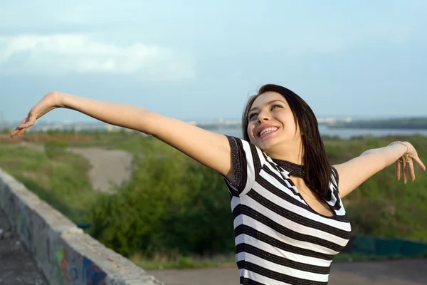 Glad ung kvinna med armar upp utomhus — Stockfoto