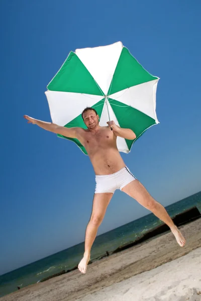 Странный молодой человек с зонтиком на пляже — стоковое фото