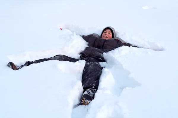 Rapaz feliz deitado na neve fresca — Fotografia de Stock