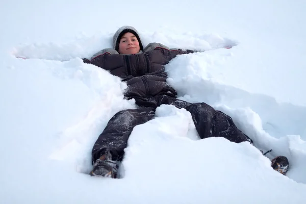Rapaz feliz deitado na neve fresca — Fotografia de Stock