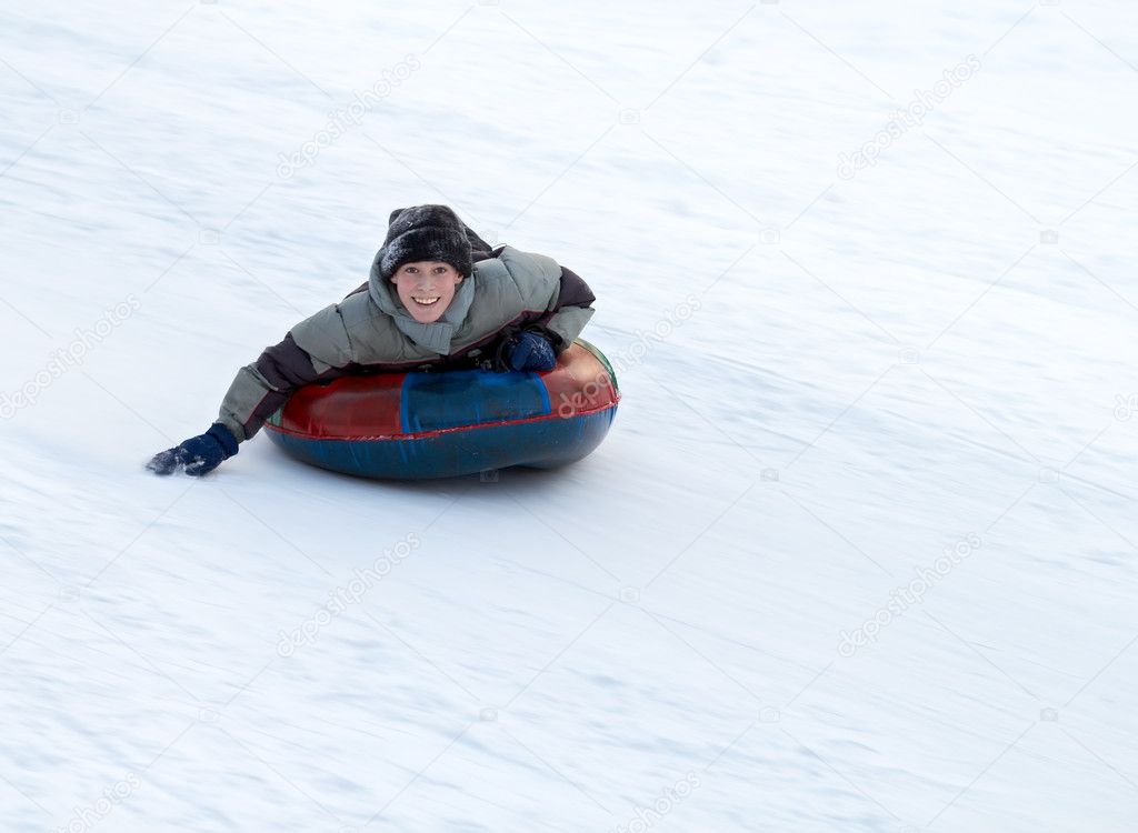 Boy sledding down a snowy hill on a color inflatable sled