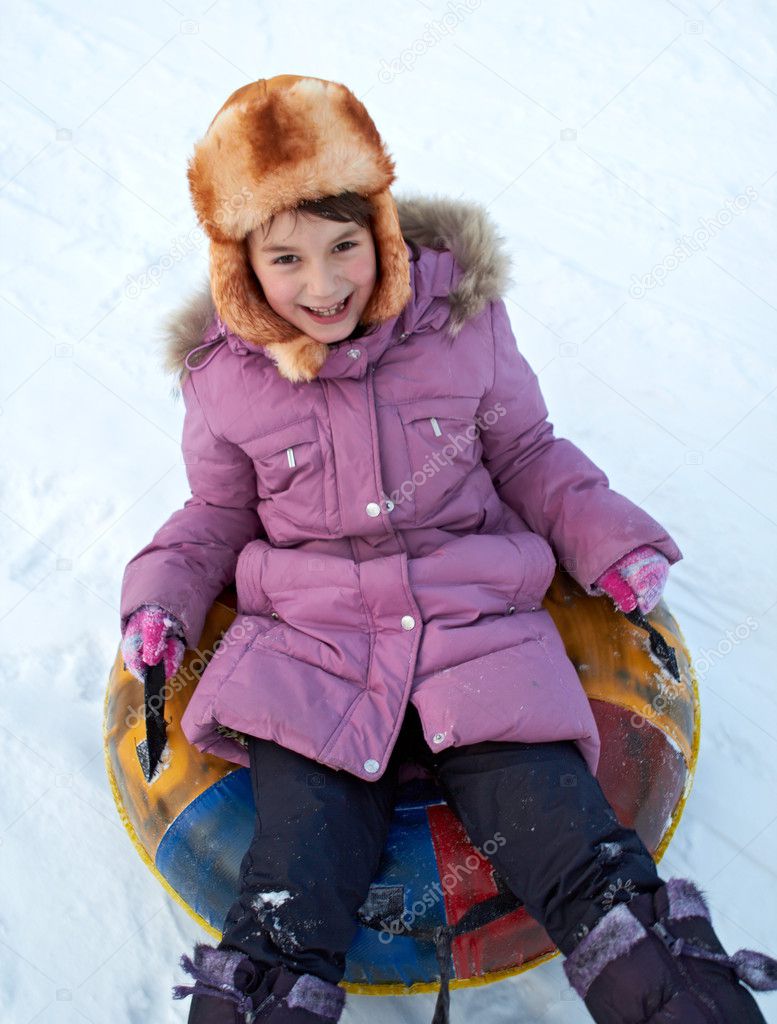 Child riding color covered inner tube down snow cover hill at speed
