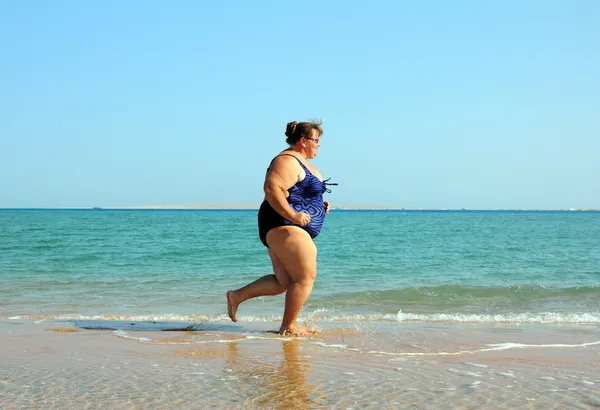 Överviktig kvinna kör på stranden — Stockfoto