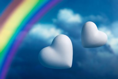 Two hearts and rainbow against a blue sky clipart