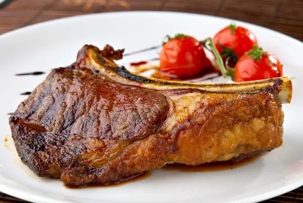 Grilled meat ribs on white plate with tomatoes — Stock Photo, Image