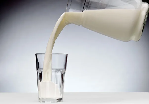Gieten van een glas melk met splash — Stockfoto
