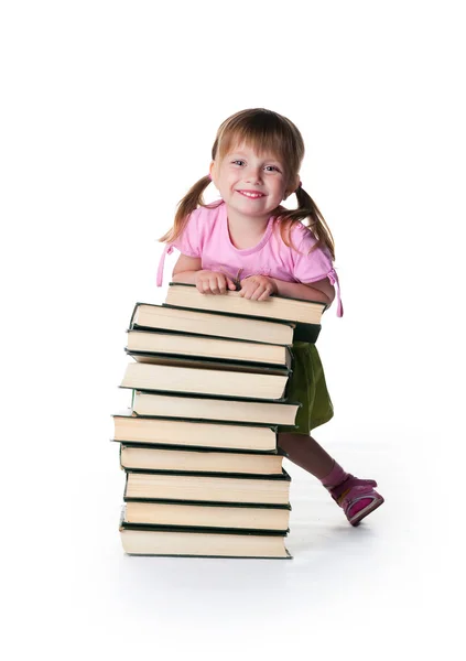 Милая маленькая девочка сидит рядом со стопкой книг — стоковое фото