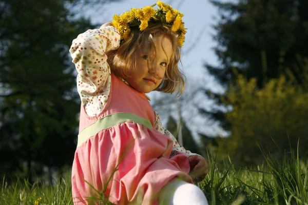 タンポポの花輪は草の上に座っている小さな女の子が笑みを浮かべて — ストック写真