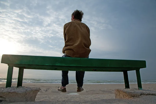 成年男子独自坐在长椅上看着惊涛骇浪的大海上独自上 — 图库照片