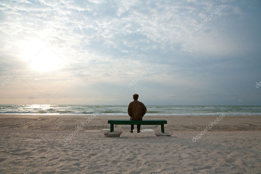Adult man sitting alone on the bench looking at a stormy sea alone