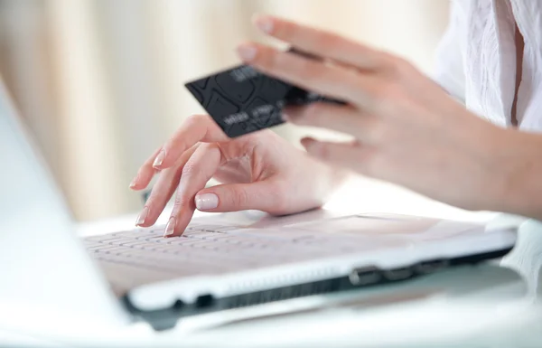 输入数据在另一只手按住一张信用卡使用笔记本电脑的女人的手 图库照片