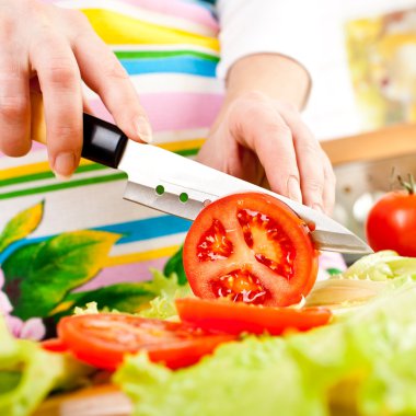 Woman's hands cutting tomato, behind fresh vegetables. clipart