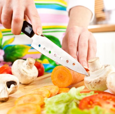 Woman's hands cutting carrot, behind fresh vegetables. clipart