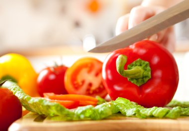 Woman's hands cutting tomato bell pepper, behind fresh vegetables. clipart