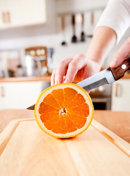 キッチンに新鮮なオレンジを切る女性の手 — ストック写真