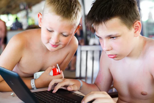 Két fiúk játszanak egy laptop a pihenés a tengerparton egy bár — Stock Fotó