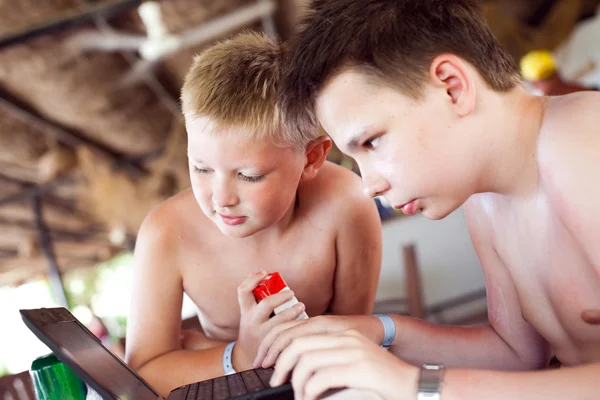 Két fiúk játszanak egy laptop a pihenés a tengerparton egy bár — Stock Fotó
