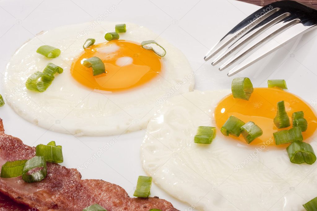 Fried eggs with fried bacon and vegetables.