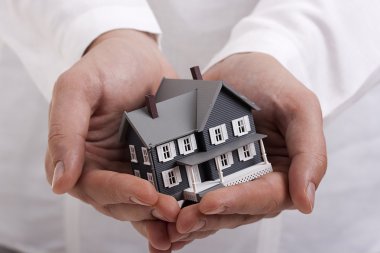 Man in white holding a model of a house in his hands. clipart