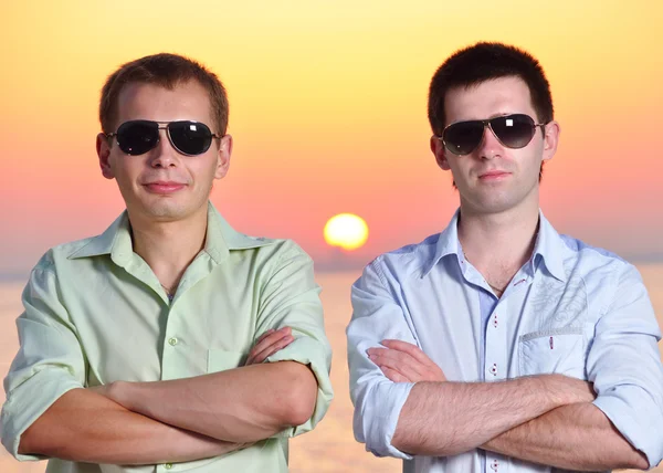 Dois amigos ao pôr-do-sol usando óculos de sol dobram os braços — Fotografia de Stock